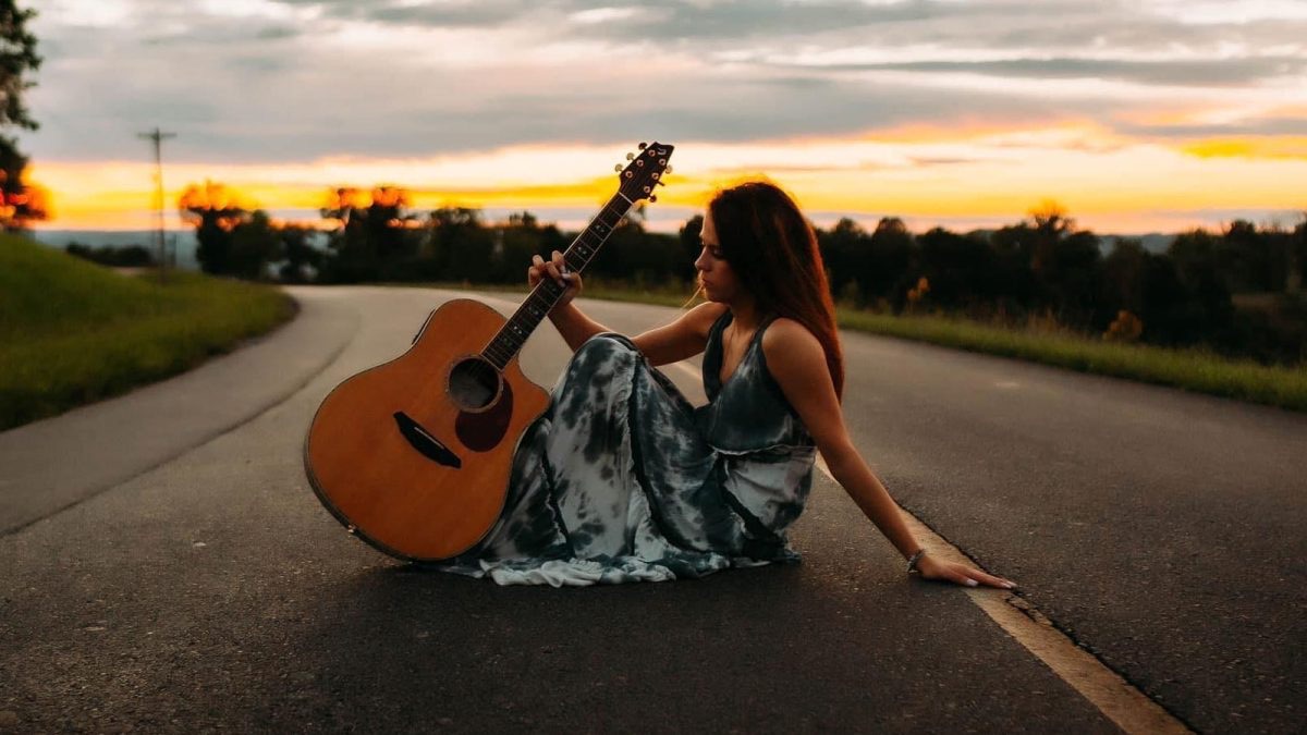 Cherokee Hope seated with an acoustic guitar at sunset